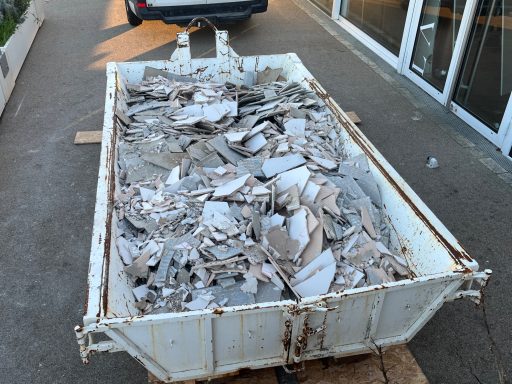 Bac à déchets rempli de débris en morceaux, situé sur un sol bétonné.