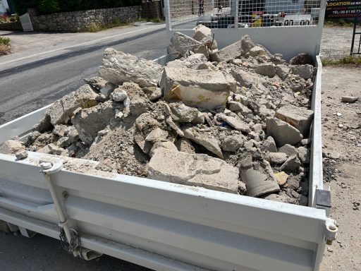 Grosses pierres et débris de béton dans une benne près d'une route.