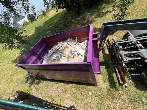 Benne de chantier remplie de déchets, posée sur un terrain vert.